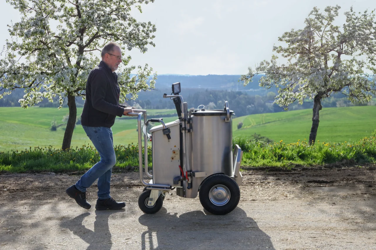 Un agriculteur tire le MilchMobil à travers un paysage idyllique et verdoyant. Entouré par la nature, il utilise l'appareil dans un environnement naturel pour nourrir ses veaux.