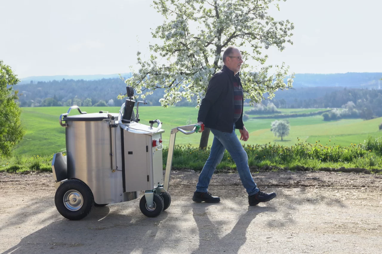 Ein Landwirt zieht das MilchMobil durch eine natürliche Umgebung, umgeben von grüner Landschaft.